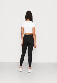 Jeans skinny pretos com bolsos traseiros, combinados com uma t-shirt branca cropped. Ténis brancos completam o visual.