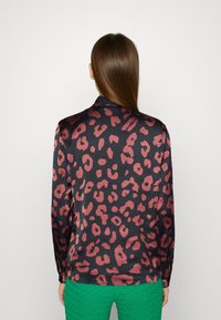 Blouse à manches longues en satin noir avec un motif léopard bordeaux. Texture lisse avec une coupe légèrement ample et un col ajusté.
