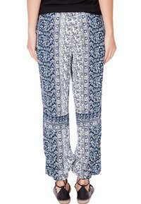 Un pantalon à motifs bleu et blanc présente un mélange de motifs floraux et de rayures. Le tissu est léger, avec des poignets élastiques et une coupe décontractée.