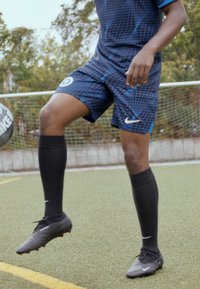 Conjunto de fútbol de Nike en azul oscuro con un patrón de rejilla, pantalones cortos negros, calcetas negras hasta la rodilla y botas negras sobre césped artificial.
