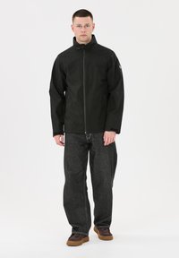 Svart vattentät jacka med hög krage, dragkedja fram och långa ärmar. I kombination med mörkgrå vida jeans och bruna skor.