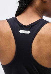 Κοντινό πλάνο στο πάνω μέρος της πλάτης ενός ατόμου που φοράει μαύρο αμάνικο τοπ με στενό κόψιμο στη πλάτη, με την ετικέτα "VENTUS 7" τοποθετημένη στο κέντρο κάτω από τον λαιμό.