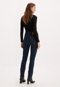 Jeans in denim blu scuro con vestibilità slim, vita alta e cuciture a contrasto. Presentano tasche posteriori e una etichetta in pelle marrone del marchio.