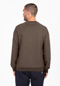 Sudadera marrón de cuello redondo con mangas raglán, puños y cintura de canalé, mostrada desde la parte trasera, con una etiqueta en el lado inferior izquierdo.