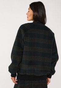 Giacca bomber a quadri in verde scuro e nero, realizzata in materiale morbido, con polsini e orlo a coste, caratterizzata da una vestibilità comoda e tasche laterali.