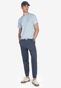 Camiseta de algodón azul claro con un gráfico pequeño; pantalones de chándal de algodón azul marino con puños elásticos; zapatillas blancas con acentos en azul y marrón.