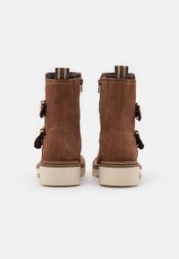 Brązowe botki zamszowe z teksturowanym wykończeniem, wyposażone w zapięcia na zamek błyskawiczny i podwójne boczne klamry. Jasnokolorowe gumowe podeszwy i paski dekoracyjne na obcasie.