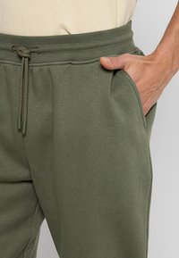 Pantalones de chándal de mezcla de algodón verde oliva con cinturilla elástica, cordón ajustable, bolsillos laterales y textura suave.
