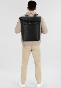 Sac à dos en cuir noir avec une poche avant, des bretelles ajustables et une poignée supérieure. Texture lisse et design minimaliste sans marquage visible.