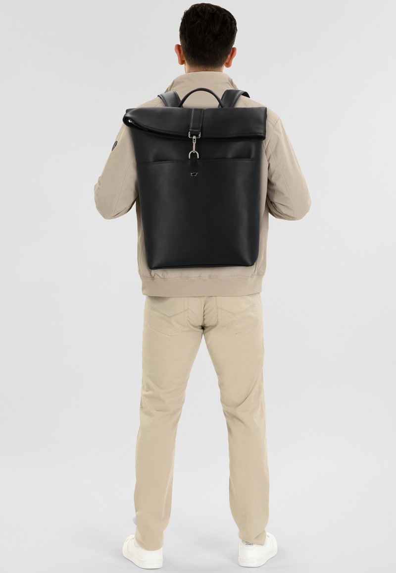 Sac à dos en cuir noir avec une poche avant, des bretelles ajustables et une poignée supérieure. Texture lisse et design minimaliste sans marquage visible.