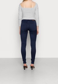 Grey long-sleeve top with a scalloped neckline paired with dark blue slim-fit jeans and black heeled mules, viewed from the back.