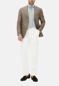 Brauner Leinenblazer, hellblaues Hemd, gemusterte blau-gelbe Krawatte, weiße Hose und dunkelbraune Wildlederschuhe.