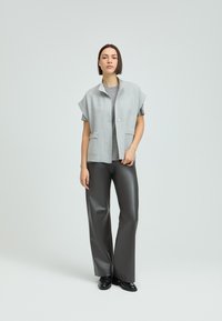 Gray sleeveless jacket with a collar, front pockets, paired with a gray textured top and black wide-leg faux leather pants.