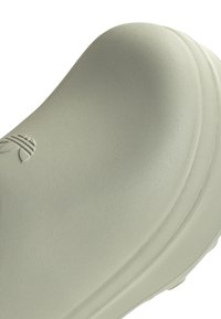 Ljusgrön gummiskor med en strukturerad yta, rundad tå och släta kanter. Har en liten präglad logotyp på sidan.