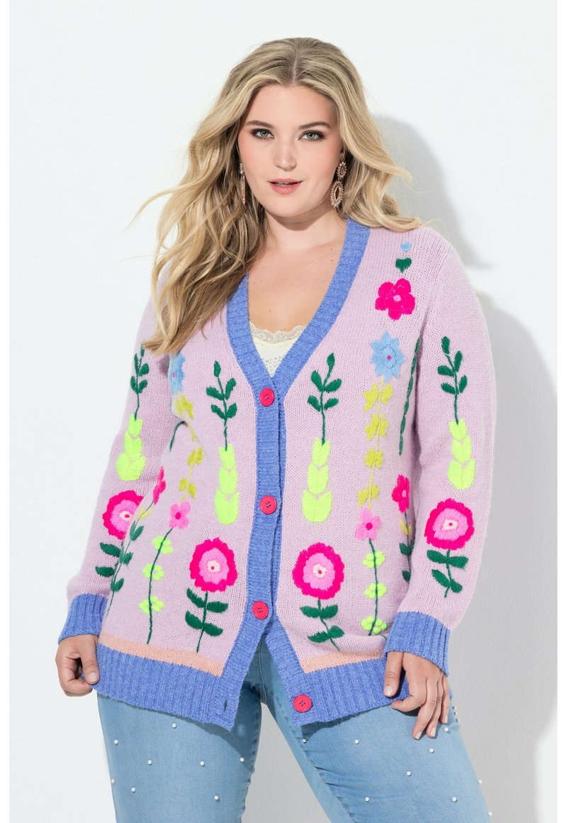 Sweter kardigan w pastelowym różu z głębokim niebieskim kołnierzem i listwą na guziki. Przód zdobią wyhaftowane kwiatowe wzory w jaskrawych kolorach.