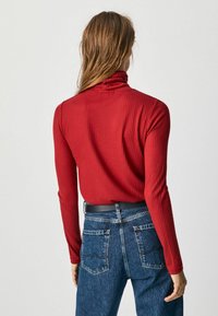 Haut à col roulé rouge à côtes avec des manches longues, associé à un jean en denim bleu taille haute avec des poches arrière et une ceinture noire.