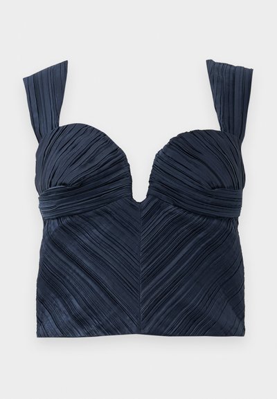 Tumesinine pleeditud lühikeste varrukatega crop top, millel on südamekujuline kaelus ja laiad rihmad; esindab vertikaalseid tekstuurijooni, luues ševroni mustri.