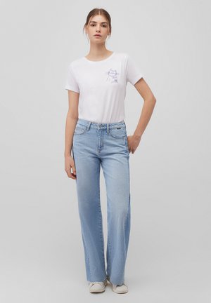 White cotton t-shirt with a lilac cat graphic on the chest, paired with light blue wide-leg jeans and white sneakers.