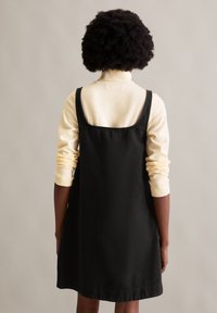 Zwarte denim jurk met een mouwloos ontwerp, featuring een ronde halslijn en zijnaden. Draagt over een lichtgele lange mouw top.