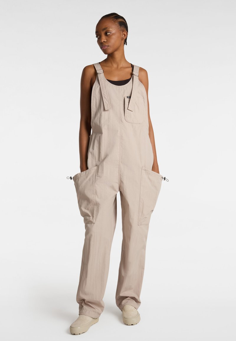 Beige Overall aus leichtem Stoff, mit großen Vordertaschen, verstellbaren Trägern und elastischen Bündchen an den Knöcheln. Lässiges Design.
