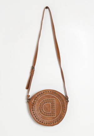 Rund brun lædertaske med justerbar rem, dekorative nitter og præget halvcirkelsmønster på fronten, hængende på hvid væg.