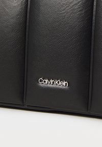 Geantă de mână din piele neagră, cu o finisare texturată, design structurat și un accent cu logo-ul argintiu Calvin Klein.