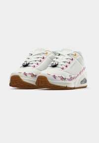 Λευκά sneakers Skechers με καφέ σόλες, πολύχρωμα σχέδια με θέμα την Ημέρα των Νεκρών και charms σε σχήμα κρανίου στα λευκά κορδόνια.
