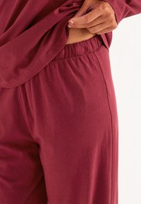 Burgundy loungekl�äder som består av en lös topp och byxor med elastiskt midjeband, tillverkade av mjukt och slätt tyg med en avslappnad passform.