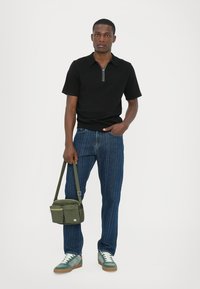 Polo scurt negru cu fermoar, blugi de denim albastri, adidași verzi cu accente albe și o geantă de umăr verde.
