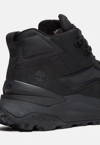 Botte de randonnée noire avec un dessus en daim texturé, des accents en mesh et une semelle en caoutchouc robuste pour la traction. Présente un logo et des œillets renforcés.