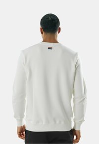 Felpa bianca a maniche lunghe con polsini e orlo a costine, caratterizzata da un piccolo dettaglio a strisce rosse, bianche e blu sulla parte posteriore del collo.