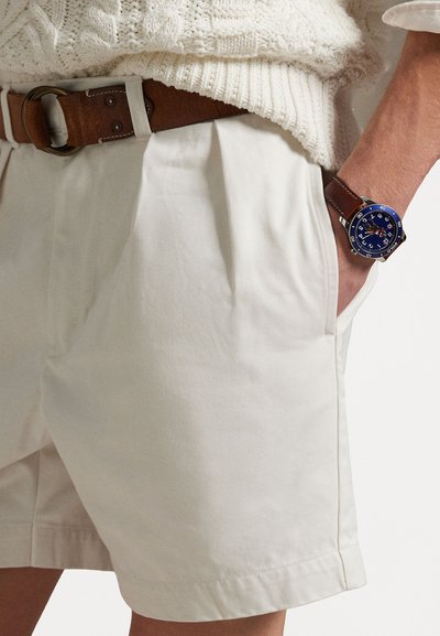 White cotton shorts with pleats, featuring side pockets. Paired with a brown leather belt and a blue-dialed wristwatch.