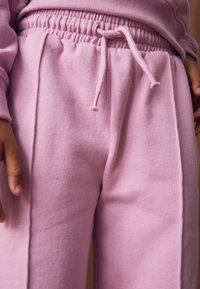 Pantalones deportivos rosas con cintura ajustable mediante cordón, confeccionados en tela texturizada. Incluyen bolsillos laterales y un corte holgado.