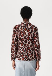 Long-sleeve shirt in silky fabric featuring a leopard print with reddish-brown and black spots on a pale pink background. Number of buttons not visible.