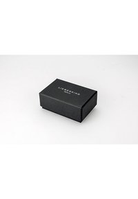 Zwarte rechthoekige doos met een gestructureerd oppervlak. De deksel heeft witte reliëftekst: "LIEBESKIND BERLIJN." Minimalistisch ontwerp, geen extra decoraties.