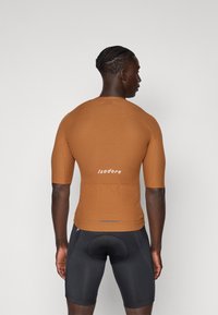 Brun kortermet syklingstrøye med ribbet tekstur og logo på baksiden. Sammen med svarte tettsittende sykkelshorts.