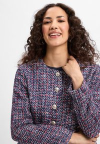 Marineblauwe en rode tweedjas met een ronde halslijn en zilveren knopen, gemaakt van textuurstof en met een getailleerd ontwerp.