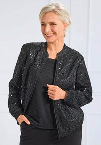 Veste bomber noire avec un design de sequins, fermeture éclair à l'avant et poignets côtelés. Associée à un haut noir texturé, elle présente une coupe décontractée.