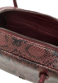 Czerwona torba ze skóry wytłaczanej w węża z zamkiem na górze. Wnętrze ma ciemne wykończenie oraz dodatkową kieszeń na zamek dla lepszej organizacji.