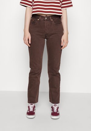 Kvinde iført brune, højtaljede jeans med lige ben, kombineret med bordeaux sneakers og en kort rød- og hvidstribet skjorte.