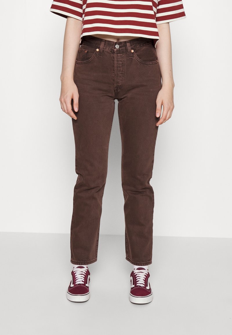 Femme portant un jean marron taille haute à jambe droite, associé à des baskets bordeaux et un haut court rayé rouge et blanc.