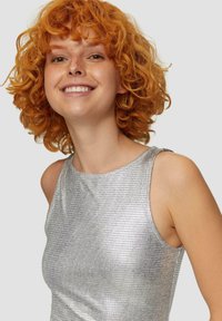 Zilveren metallic tanktop met een gestructureerd ruitpatroon, voorzien van een ronde halslijn en een mouwloos ontwerp, gecombineerd met een krullend oranje kapsel.
