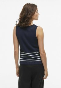 Maglione senza maniche di colore blu navy con strisce orizzontali bianche lungo il fondo. Texture liscia, scollatura a costine e design aderente.