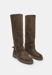 Stivali alti in suede marrone con punta rotonda, zip laterale e due cinghie decorative con fibbie. Suola piatta e superficie testurizzata.