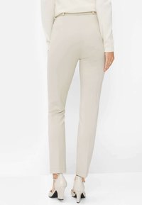 Beige Slim-Fit-Hosen mit glatter Textur, die eine mittelhohe Taille und ein nahtloses Design aufweisen, kombiniert mit hellen Stilettos.