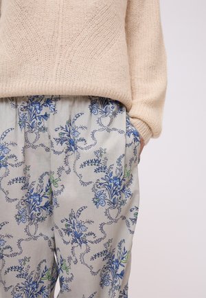 Maglione lavorato a maglia beige sopra pantaloni chiari grigi con motivo floreale che presenta fiori blu e verdi, vestibilità ampia con tasche laterali.