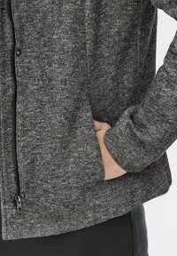 Grå tekstureret jakke med lynlås foran, sidelommer og en tætsiddende pasform. Blødt stof med et diskret meleret mønster og et simpelt design.