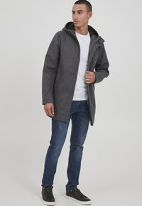 Grau, Wollmischung Mantel mit Kapuze, Reißverschluss und Seitentaschen. Kombiniert mit einem weißen T-Shirt und ausgewaschenen blauen Jeans, abgerundet mit schwarzen Turnschuhen.