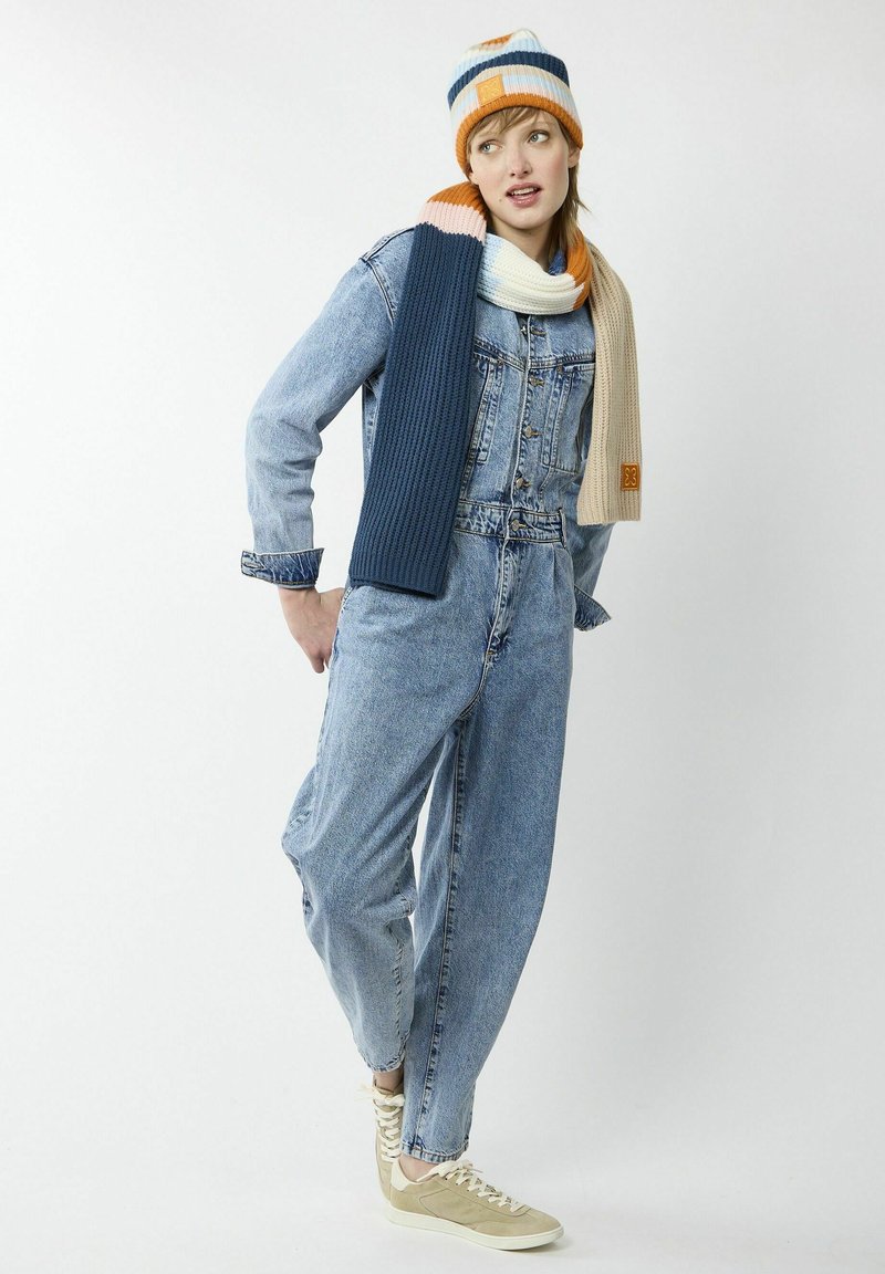 Jeansoverall met lange mouwen, blauwe kleur en een lichte wassing, gecombineerd met een gestreepte gebreide muts en sjaal in oranje, blauw en crème.