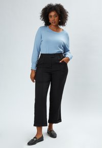 Maglione azzurro chiaro, pantaloni neri a vita alta con tasche, scarpe nere flat, tessuto texturizzato, vestibilità rilassata, orlo dei pantaloni a sbuffo.